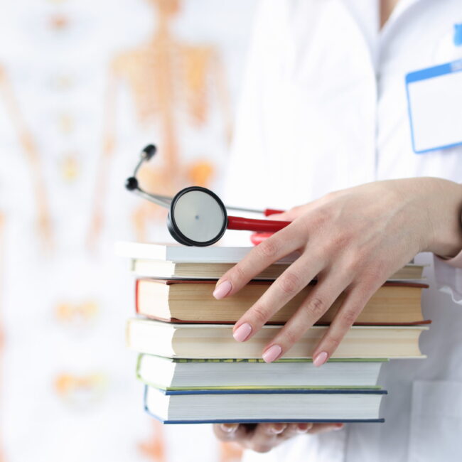 Doctor hands are holding stack of books and stethoscope. Medical education concept